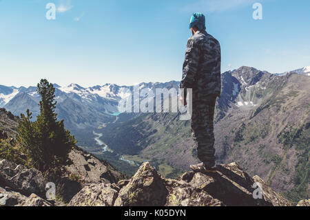 Silhouette of a man standing on the mountain top and looking into the distance on a beautiful mountain lake. The guy in camouflage sneaking through th Stock Photo