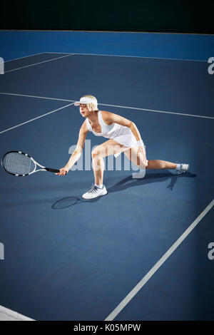 Young female tennis player playing tennis, reaching with tennis racket on blue tennis court Stock Photo
