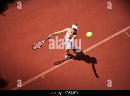 Overhead view young female tennis player playing tennis, serving the ball on sunny clay tennis court Stock Photo