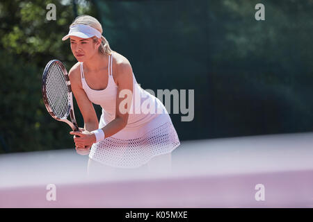 Focused young female tennis player ready, holding tennis racket on sunny tennis court Stock Photo