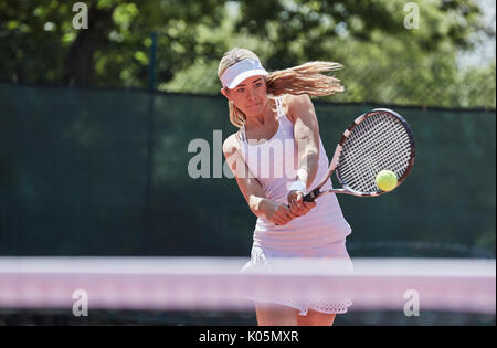 Determined young female tennis player playing tennis, hitting the ball on sunny tennis court Stock Photo