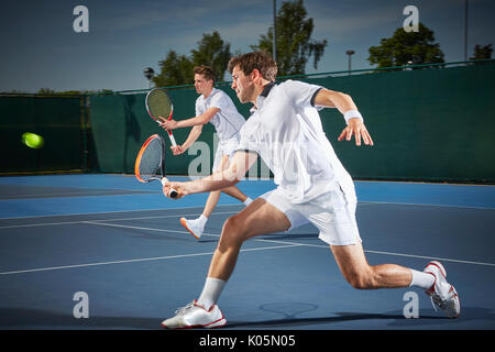 Young male tennis doubles players playing tennis, hitting the ball on blue tennis court Stock Photo