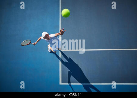 Overhead view of young male tennis player playing tennis, serving the ball on sunny blue tennis court Stock Photo