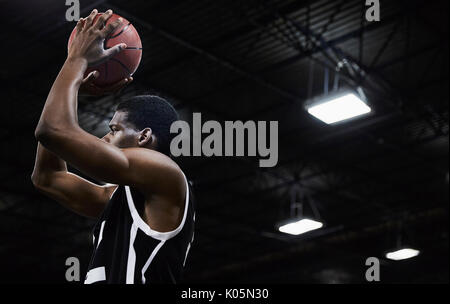 Focused young male basketball player shooting the ball in gymnasium Stock Photo