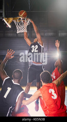 Young male basketball player dunking the ball into hoop with defenders below Stock Photo