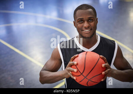 Portrait smiling young male basketball player holding basketball on court Stock Photo
