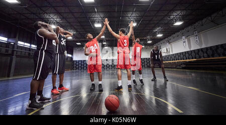 Young male basketball players high-fiving, celebrating on court in gymnasium Stock Photo