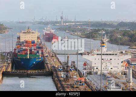 Panama Canal, Panama.  Two Ships Entering First Lock Heading South, Caribbean in far rear.  Third Ship Awaits its Turn.  Colon Port Cranes in far Back Stock Photo