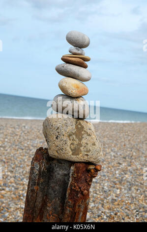 pile of pebbles balancing on rusty metal post, cley, north norfolk, england Stock Photo