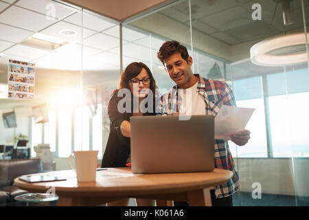 Young businessman and businesswoman working together on laptop in office. Couple of creative professionals working on new project. Stock Photo