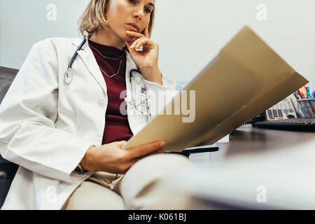 Doctor reading medical documentation in hospital. Female physician sitting in her office and examining medical records. Stock Photo