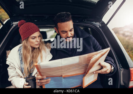Young couple using a map on a road trip for directions. Young man and woman reading a map while sitting at the back of car. Stock Photo