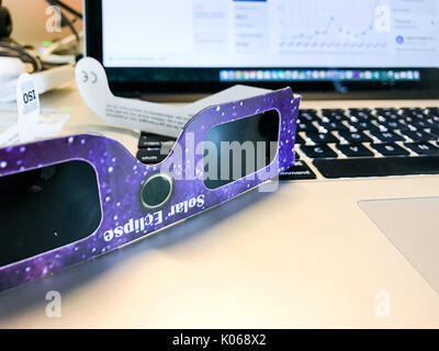 A working employee has eclipse glasses by a computer - clouds and busy schedules kept millions of employees from witnessing the solar event Stock Photo