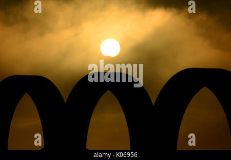 Partial Eclipse viewed briefly through hazy cloud over the silhouette of the Olympic Rings, Portland, Dorset, UK Credit: Finnbarr Webster/Ģ����ý Live News Stock Photo
