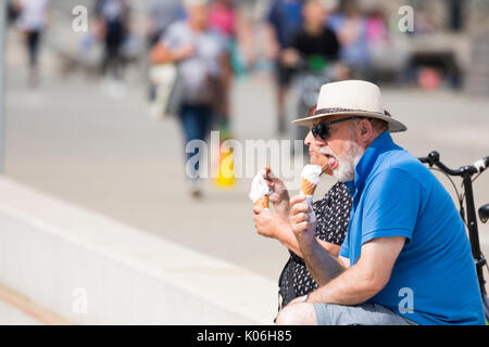 Mature couple retired enjoying a cooling ice cream and cone sat down on the promende on a summer day at the coastal resort seaside town of Colwyn Bay in North Wales, UK Stock Photo