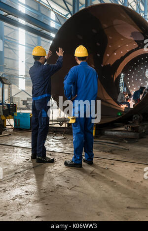 Workers supervising the manufacture of a metallic cylinder  Stock Photo