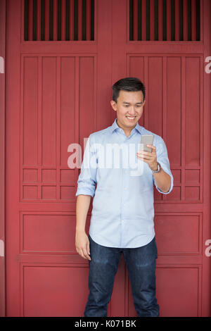 Chinese business Man using his Smart phone outdoors in Asian city. Asian businessman using his smart phone with Red doors of Chinese heritage building Stock Photo
