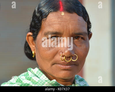 Mature Indian Adivasi woman with red sindoor, three golden nose rings and tribal earrings. Stock Photo