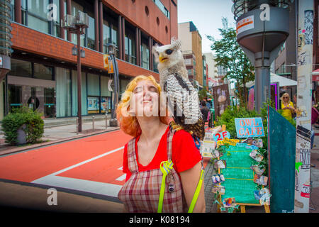 TOKYO, JAPAN JUNE 28 - 2017: Beautiful owl posing over a smiling woman shoulder in the street in Akihabara owl cafe - owls are very popular pets in Japan Stock Photo