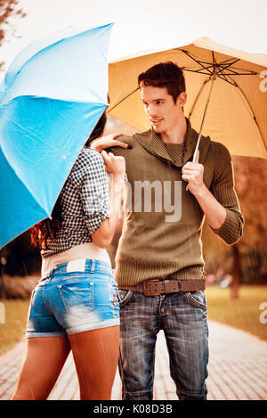 Beautiful lovely couple with umbrellas enjoying while walking in the rain through the park in autumn colors. Stock Photo