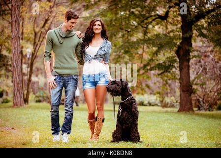 Beautiful lovely couple with a black giant schnauzer, enjoying and walking in the park. Stock Photo