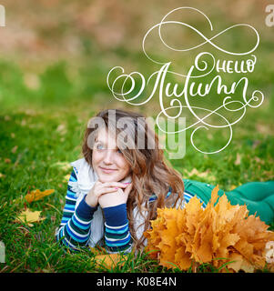 Hello Autumn calligraphy lettering text. Young beautiful girl in autumn park with a wreath of yellow leaves on the head Stock Photo