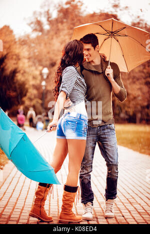 Beautiful lovely couple enjoying and dancing with umbrellas in the park in autumn colors. Stock Photo