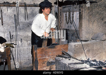 A male interpreter in period clothing plays the role of a blacksmith in the historic Colonial Quarter in St. Augustine, Florida, USA, where early Spanish and British life in America is portrayed for visitors. The man is operating a bellows to heat the metal implements he is making. St. Augustine claims to be the nation's oldest continuously inhabited city since its founding as a Spanish territory in 1565. Stock Photo