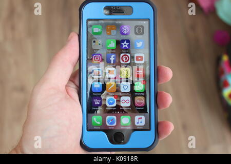 iPhone with a protective blue cover from Anker held in a mans hand showing apps and notifications on the screen Stock Photo