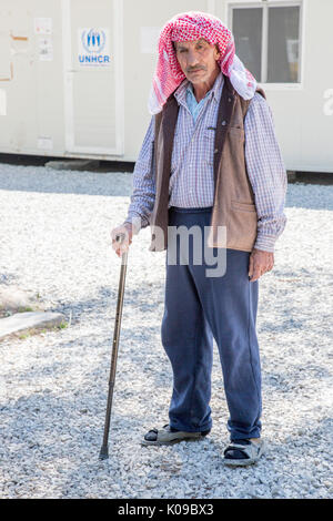 An older Syrian man supported by a walking stick stands in front of a prefabricated office building with a UNHCR sign. UN High Commission for Refugees Stock Photo