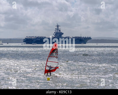 A windsurfer sails on the Solent in front of the US Navy aircraft carrier USS George H W Bush. Stock Photo