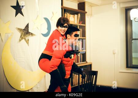 Two college students dressed as characters from the movie 'The Incredibles' are posing for a picture in front of a cloth with large stars and a moon on it, the girl is looking towards the camera and is receiving a piggy back ride from the boy, while the boy is looking in another direction, 2015. Courtesy Eric Chen. Stock Photo