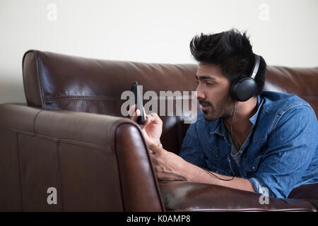 Asian man lying on the sofa sending a text message and listening to music Stock Photo