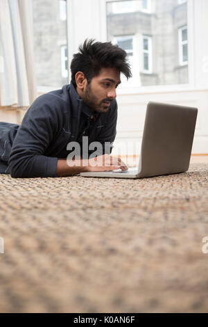 Asian Man lying on floor at home and using a laptop. Stock Photo