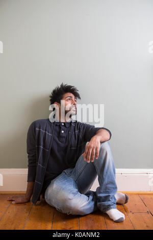 Portrait of a happy Indian man sitting on floor against green wall. Stock Photo