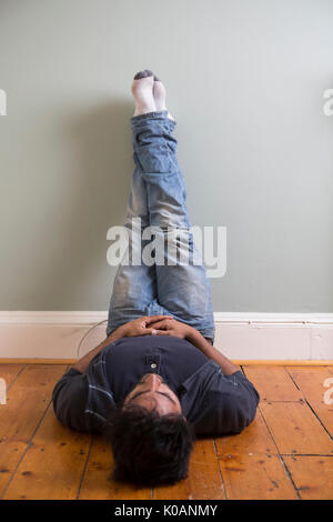 Portrait of a happy Indian man sitting on floor against green wall. Stock Photo
