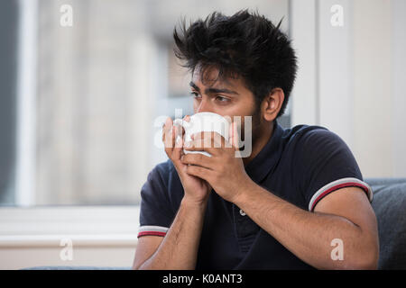 Portrait of a Asian man at home drinking a hot mug of coffee or tea. Stock Photo
