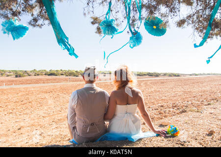 Newlywed couple sitting under shade of tree in summer Stock Photo