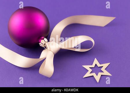 Beautiful purple christmas ball with satin effect, grey gift ribbon and metallic silver stars on purple background. Stock Photo