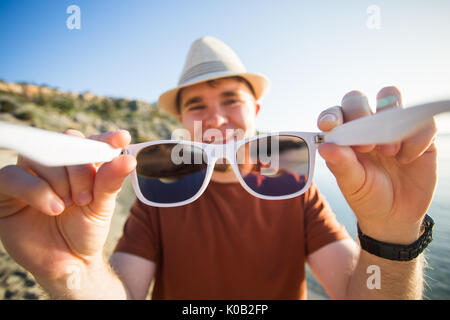 Handsome young man puts on camera sunglasses on the beach. Travel, fun, summer and vacation concept Stock Photo