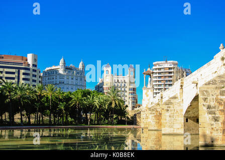 A historic stone bridge Puente Del Mar and a pond near it with residential apartment buildings and a row of palms in the center of Valencia, Spain on  Stock Photo