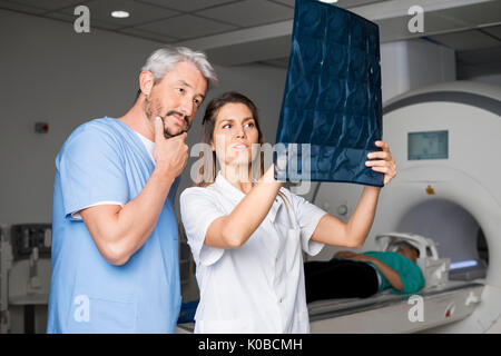 Doctors Examining X-ray With Patient Lying On CT Scan Machine Stock Photo