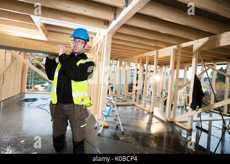 Carpenter In Protective Jacket Carrying Wood On Shoulder At Site Stock Photo