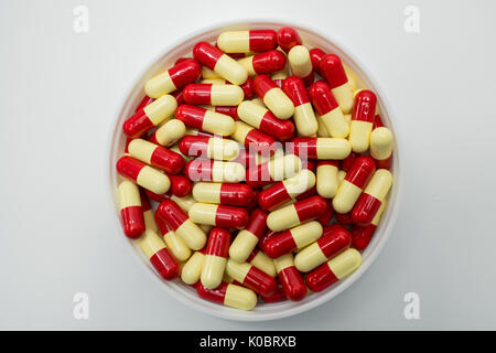 Top view of red, pale yellow, capsule pills in plastic container on white background Stock Photo