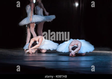 dancing, agility, beauty concept. thin and adorable female ballet dancers dressed in shiny white tutus and leotards, they are lying on the stage of the theater with their arms folded Stock Photo
