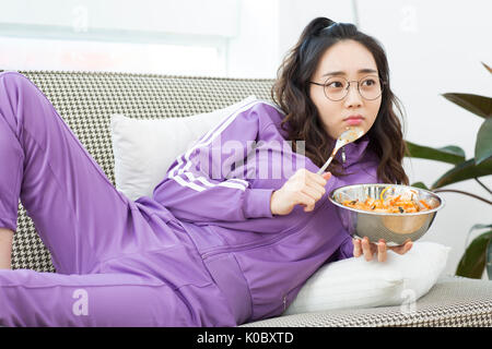 Young NEET woman watching TV eating meal Stock Photo
