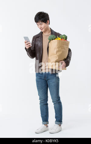 Young smiling man with shopping bag standing using smartphone Stock Photo