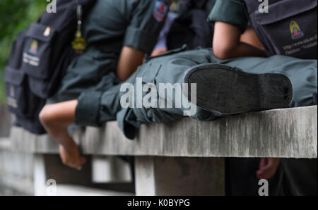 Schoolboys wear military students uniform sleeping on a bench made of cement in school among their friends standing nearby Stock Photo