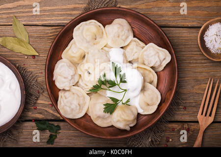 Homemade meat dumplings - russian pelmeni with sour cream and parsley close-up, top view Stock Photo