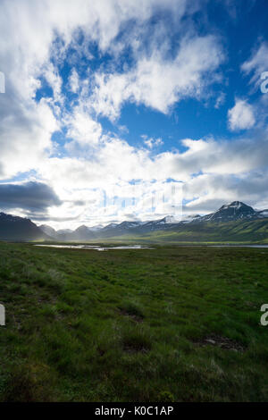 Iceland - Endless magical landscape with sunny green meadows between snowy mountains Stock Photo